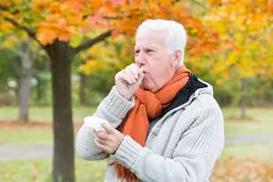 Senior man coughing at park on fall day