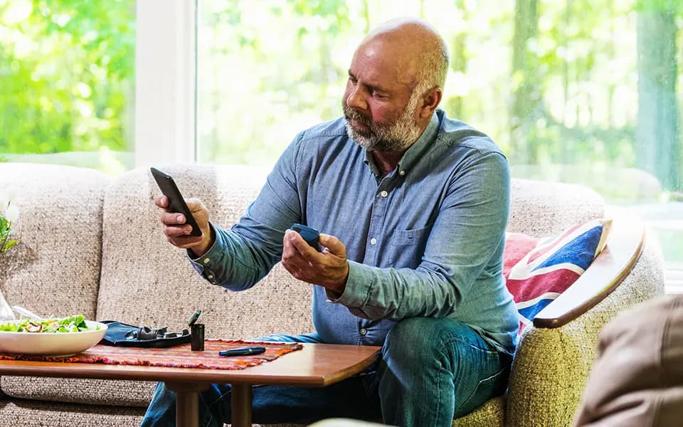 Older man testing blood and checking smartphone