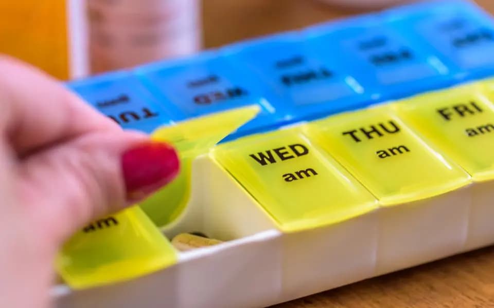 Woman with red fingernail polish using a weekly pill organizer for medication management