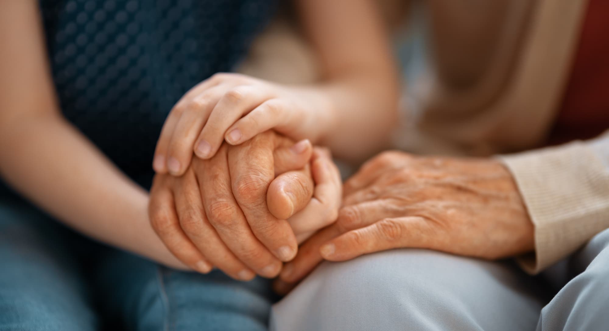 A younger adult holding a senior's hands in their lap