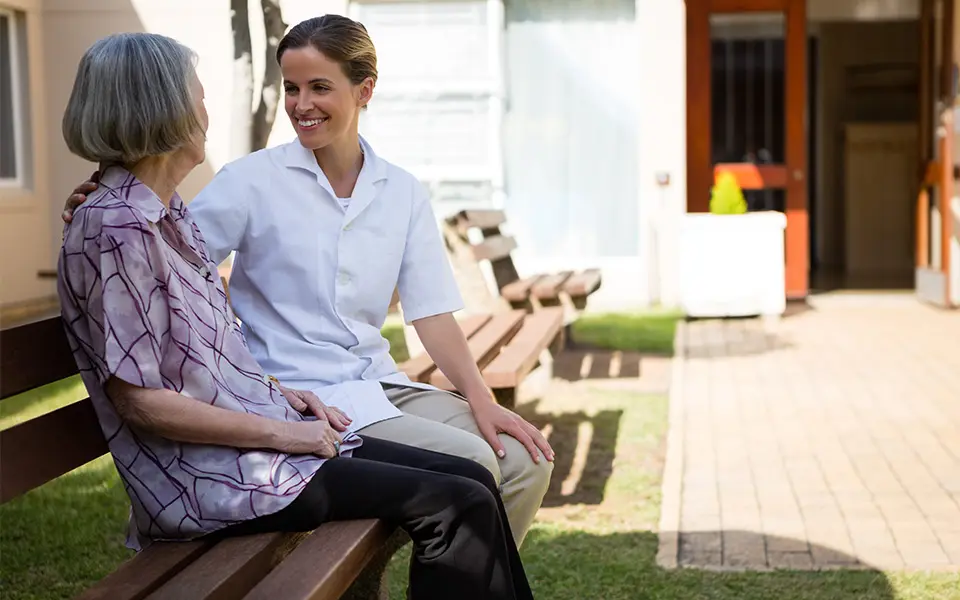 Senior woman talking to doctor while sitting on bench at an assisted living facility