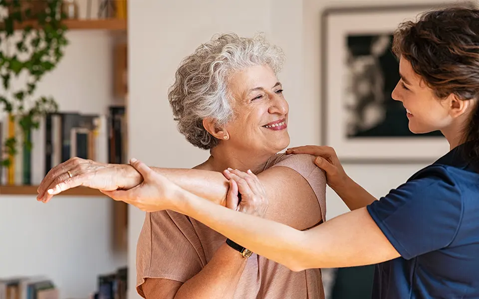Nurse helping an elderly woman do physical therapy at home