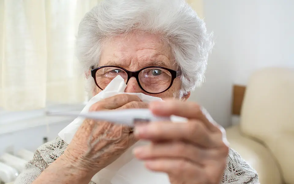Sick senior woman checking body temperature with thermometer and holding a tissue paper over her face