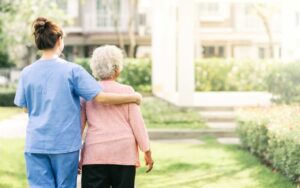 nurse caregiver support walking with elderly woman outside of a memory care facility